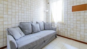 A room with a grey sofa, tiled walls, a window with sheer curtains, and a corkboard on the wall. - Welc-oM Prato della Valle (Padova)