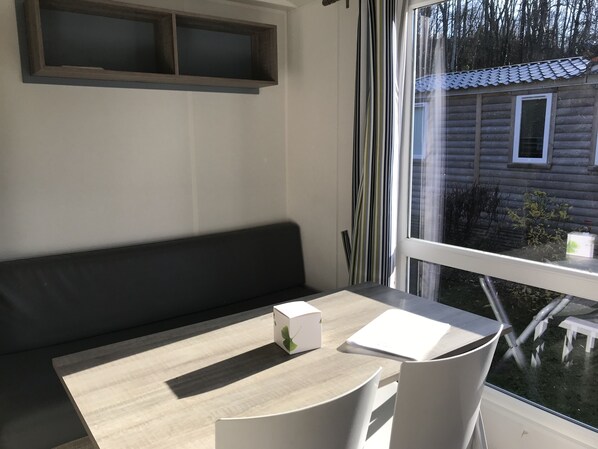 A room with a wooden table, white chairs, a black bench, and a window with curtains. - Mobile-home Camping Ser Sirant (Saint-Theoffrey)
