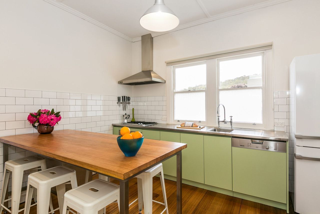 A kitchen with a wooden table, bar stools, a sink, and a dishwasher.