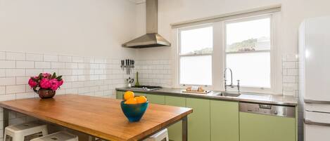 A kitchen with a wooden table, bar stools, a sink, and a dishwasher.