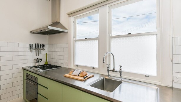 Eine Küche mit einem Edelstahlherd, einem eingebauten Backofen, einem Fenster mit Milchglas und einem grünen Schrank.
