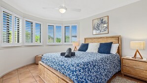 A bedroom with a large bed, a ceiling fan, and multiple windows with shutters. - SHORELINE 3 BEACH FRONT APARTMENT (HASTINGS POINT)
