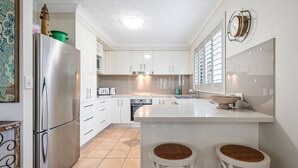 A modern kitchen with white cabinets, a stainless steel refrigerator, a built-in oven, and a large island with stools. - SHORELINE 3 BEACH FRONT APARTMENT (HASTINGS POINT)