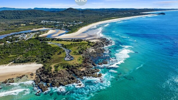 An aerial view of a coastal area with a beach, rocky shoreline, and a road leading to a parking area. - SHORELINE 3 BEACH FRONT APARTMENT (HASTINGS POINT)