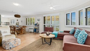 A spacious living area with a dining table, a sofa set, and a kitchen in the background. - SHORELINE 3 BEACH FRONT APARTMENT (HASTINGS POINT)