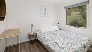 A bedroom with a bed, a bedside table, a lamp, a picture on the wall, and a window with a view of the outdoors.