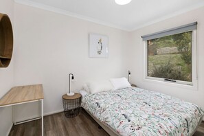 A bedroom with a bed, a bedside table, a lamp, a picture on the wall, and a window with a view of the outdoors. - Hull's Haven (Wye River)