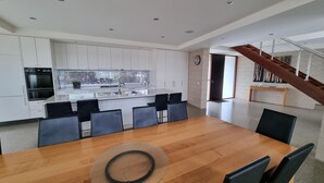 Eine moderne Küche mit weißen Schränken, einer zentralen Kochinsel und einem Essbereich mit einem Holztisch und schwarzen Stühlen.