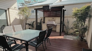 A patio with a glass table and chairs, a barbecue grill, and potted plants.