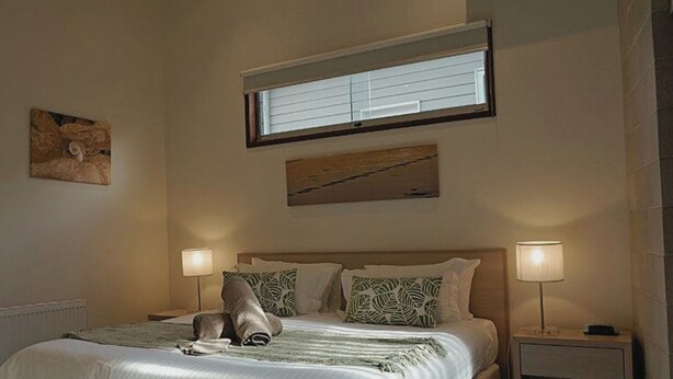 Ein Schlafzimmer mit einem Bett, zwei Nachttischlampen, einem Fenster mit Jalousien und zwei Wandbildern.