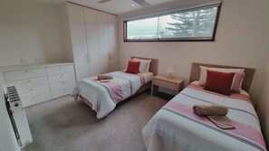 A bedroom with two beds, a wardrobe, a window, and a bedside table with a lamp.