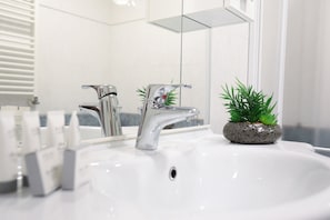 A bathroom with a white sink, chrome faucets, and a small potted plant.