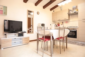 A modern kitchen with a built-in oven, a dining table with chairs, and a television on a white cabinet.