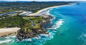 Vista aérea de una zona costera con playa, costa rocosa y una carretera que conduce a un estacionamiento.