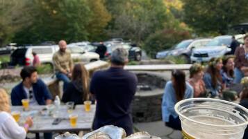 A dining table with oysters and a beer cup, set outdoors with people in the background.