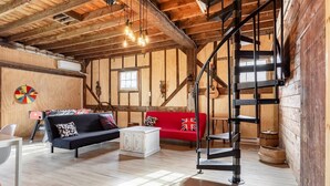 Un interior rústico con vigas de madera a la vista, una cama en altillo, un sofá rojo, un armario blanco y una mesa de futbolín.
