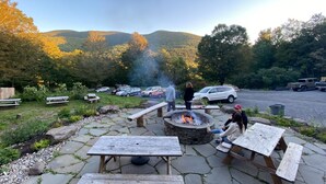 Un patio al aire libre con piso de piedra, mesas de picnic y una chimenea central.