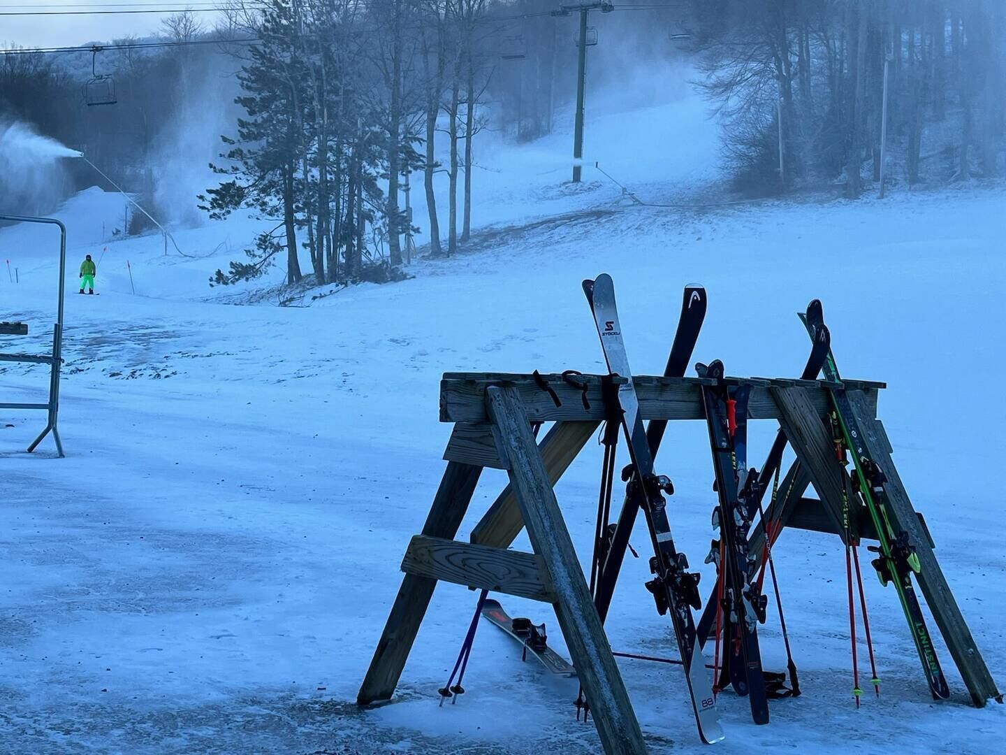 A wooden ski rack with skis and poles in a snowy outdoor setting.