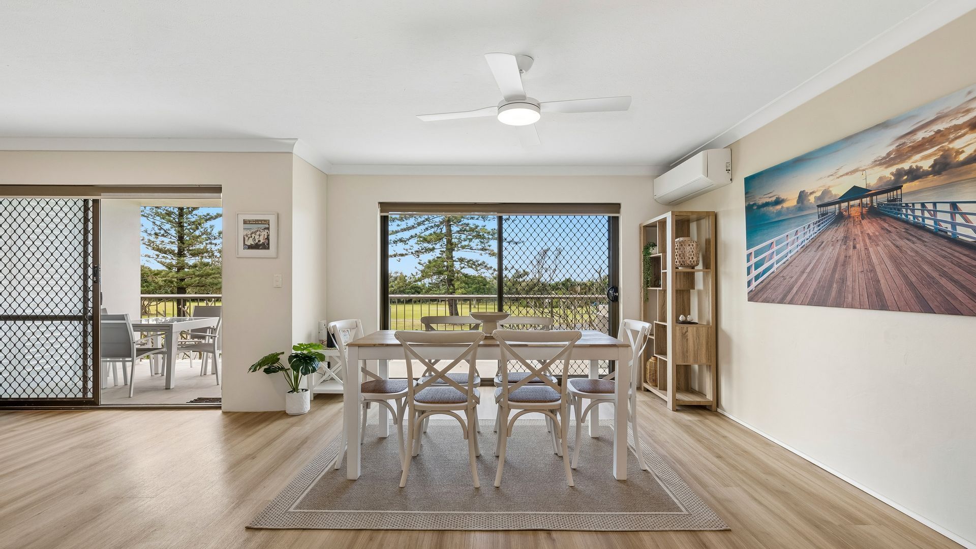 A dining area with a table and chairs, a ceiling fan, and a view of the outdoors through large windows.