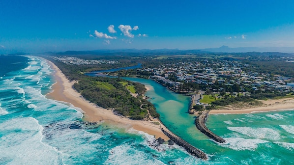 An aerial view of a coastal town with a beach, a river, and residential areas.