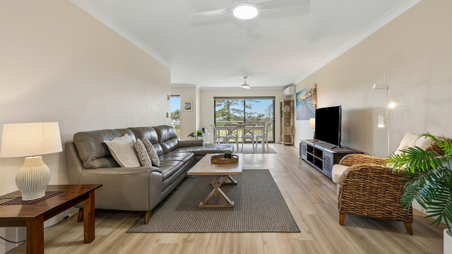 A modern living room with a leather sofa, a TV, and a dining area with a table and chairs.