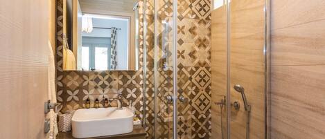 A bathroom with a glass-enclosed shower, a sink with toiletries, and patterned tiles.