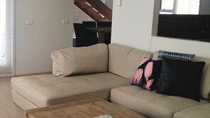 A beige sectional sofa with a wooden coffee table in a living room with a staircase in the background. - Lonsdale Shores in Point Lonsdale (Point Lonsdale)