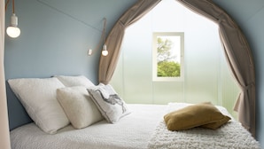 Ein Schlafzimmer mit Bett, Kissen, einem Fenster und einem Vorhang.