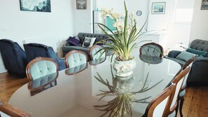 A modern living room with a glass-top dining table, surrounded by upholstered chairs, a sofa, and a potted plant. - Ozone Tower in Queenscliff (Queenscliffe)