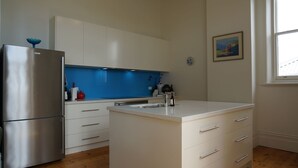 A modern kitchen with a stainless steel refrigerator, white cabinets, a blue backsplash, and a small island with a sink. - Ozone Tower in Queenscliff (Queenscliffe)