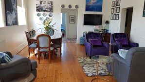 A living room with a dining area, two purple armchairs, a glass coffee table, and a TV mounted on the wall. - Ozone Tower in Queenscliff (Queenscliffe)