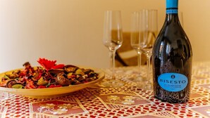 Eine Flasche Bistec Wein, ein Teller Essen und drei Gläser auf einem Tisch mit kariertem Tischläufer.
