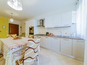 A modern kitchen with white cabinets, a gas stove, and a sink. There is a dining table with a lace tablecloth and chairs.