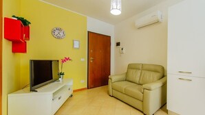 Ein Wohnzimmer mit einer Couch, einem Fernseher auf einem weißen Schrank, einer Uhr und einer Tür.