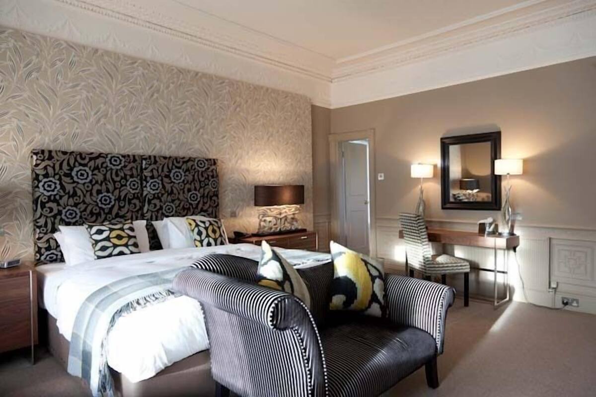 A hotel room with a large bed, a sofa, a desk, and a mirror.