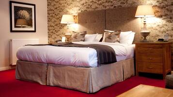 A neatly made bed with a red carpet, two bedside lamps, a wooden nightstand, and a framed picture on the wall.