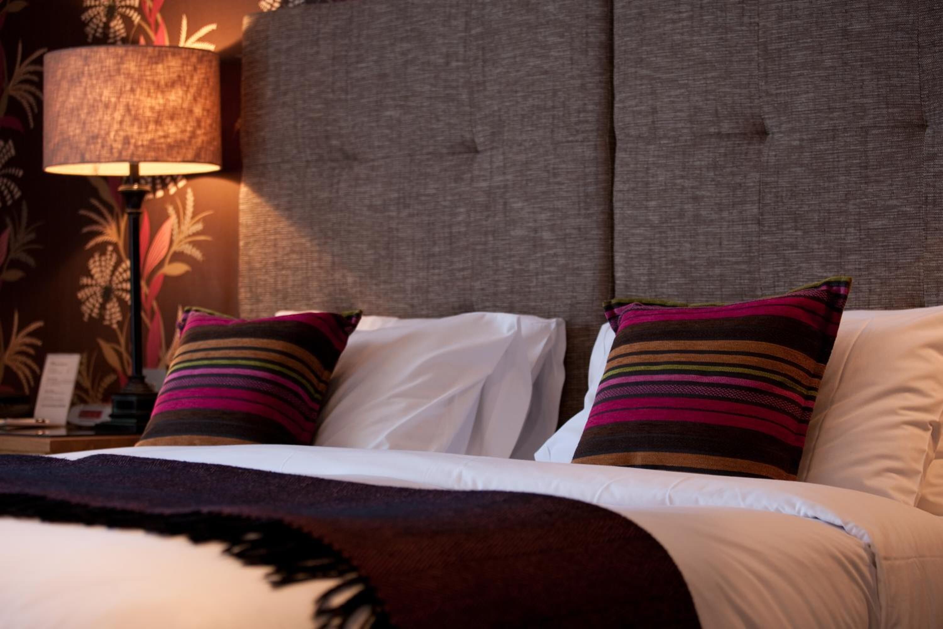A hotel room with a large bed, a headboard, and a nightstand with a lamp.
