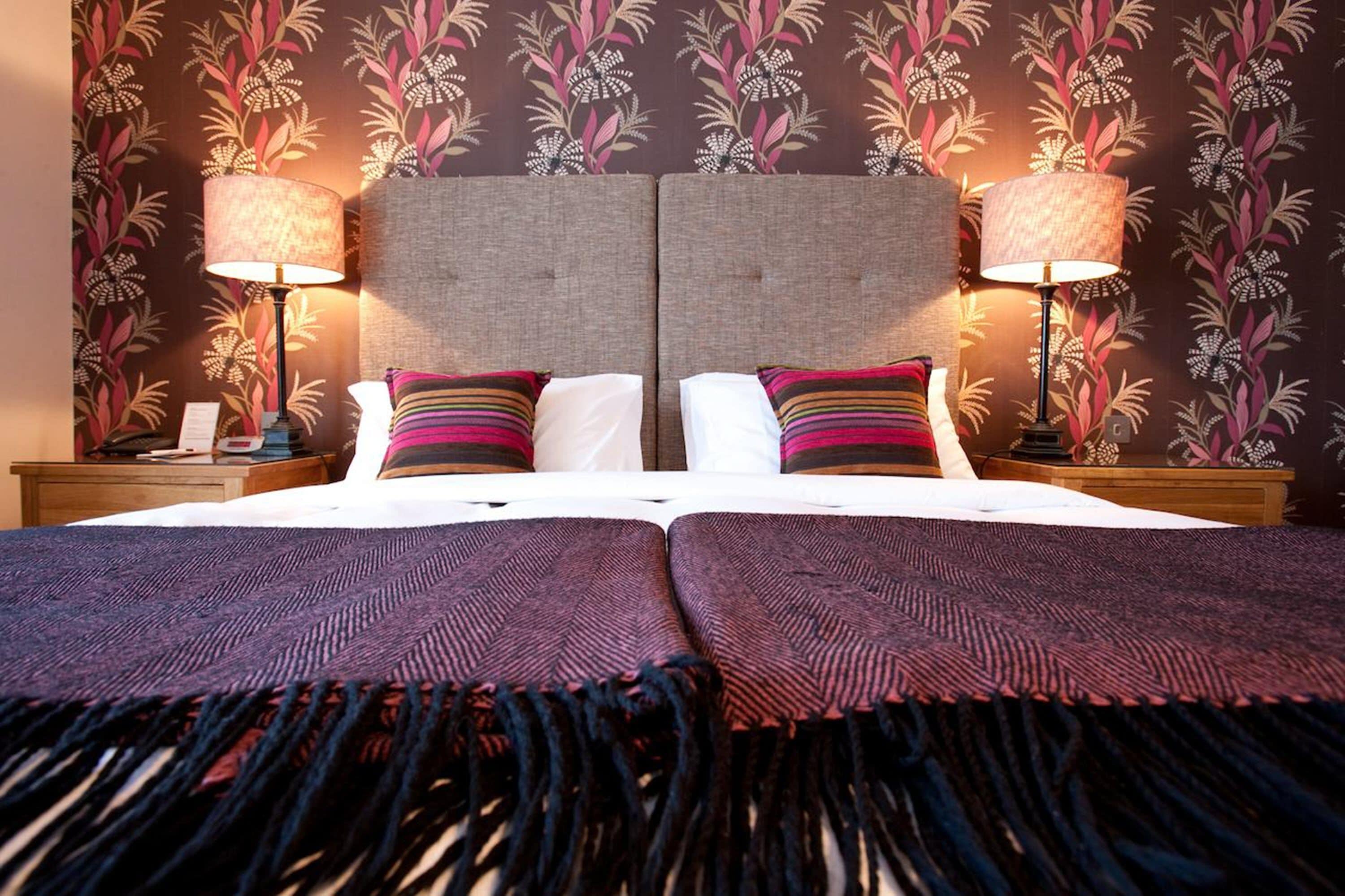 A double bed with two pillows, a headboard, and two bedside lamps.