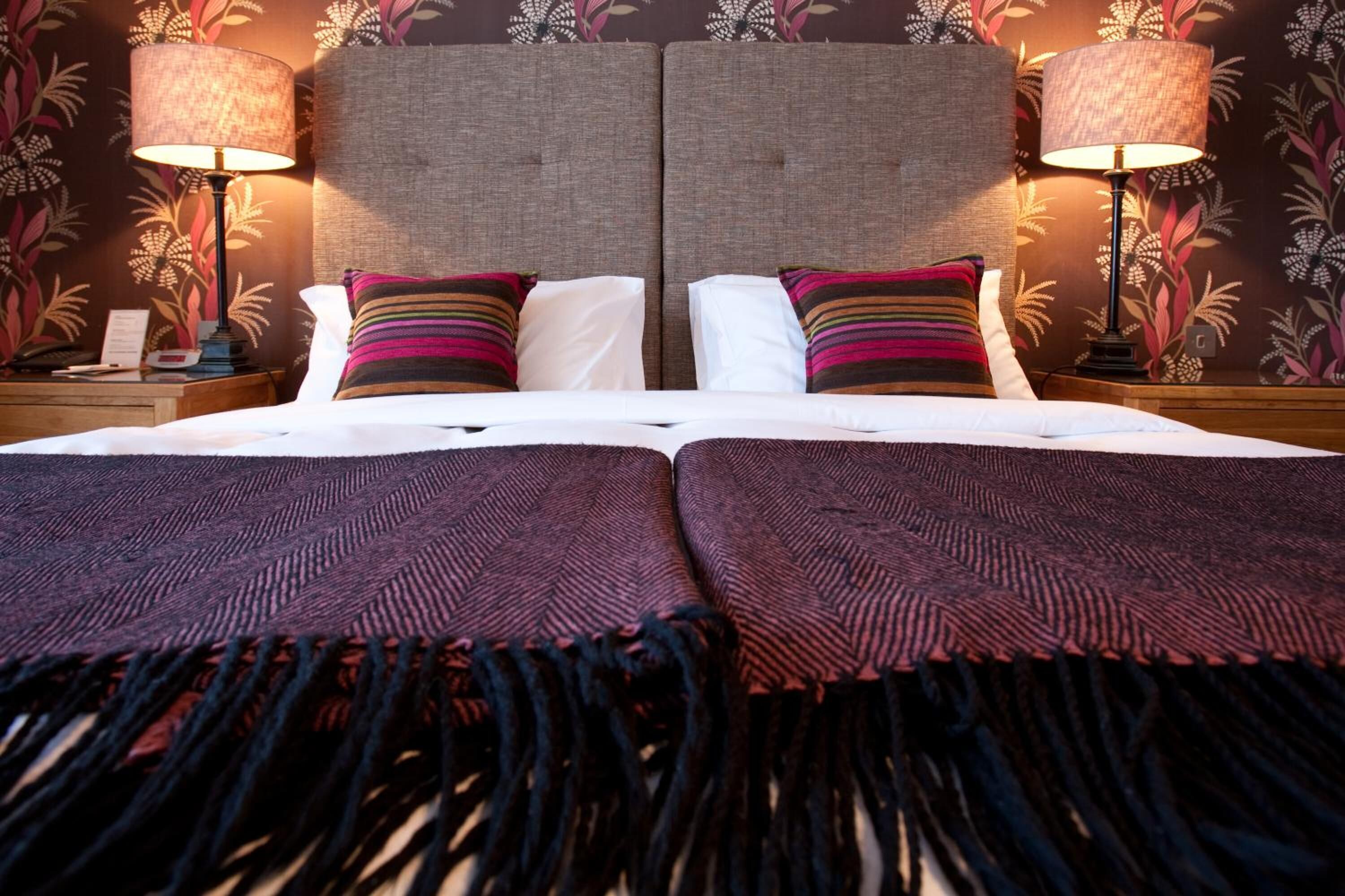 A double bed with a headboard, two bedside lamps, and a floral wallpaper pattern.