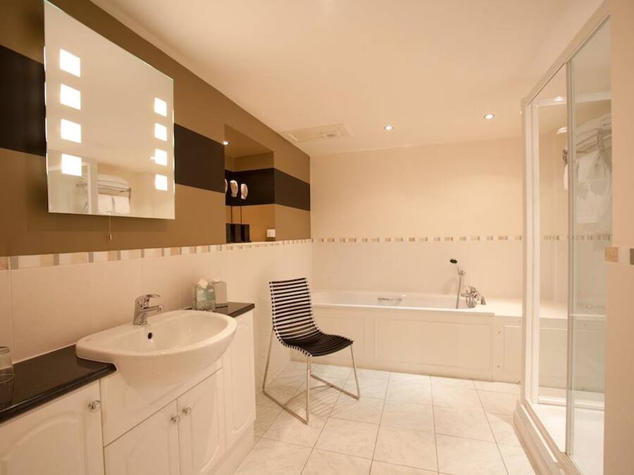 A bathroom with a large mirror, a sink, a chair, and a bathtub.
