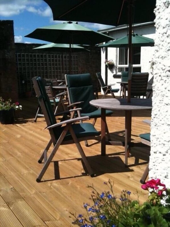 An outdoor patio with wooden flooring, green cushioned chairs, and a round table.