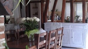 Ein rustikaler Essbereich mit Holzkohlenstühlen und einem Tisch, umgeben von Topfpflanzen und einem weißen Schrank.