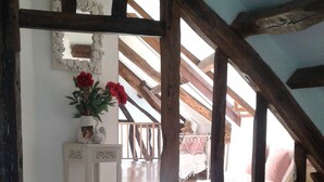 Ein rustikaler Raum mit freiliegenden Holzbalken, einer Treppe zu einem Balkon und einem Bett mit Blumenmuster-Bettdecke.
