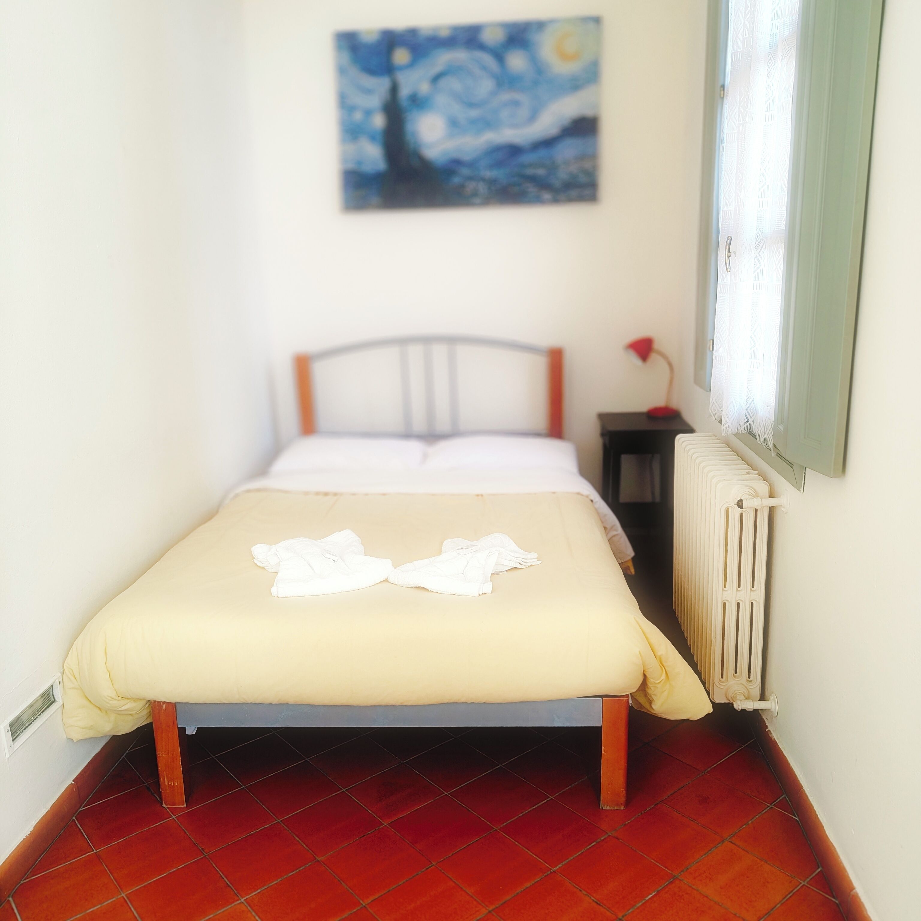 Een klein, verzorgd bed in een kamer met een radiator en een schilderij aan de muur.