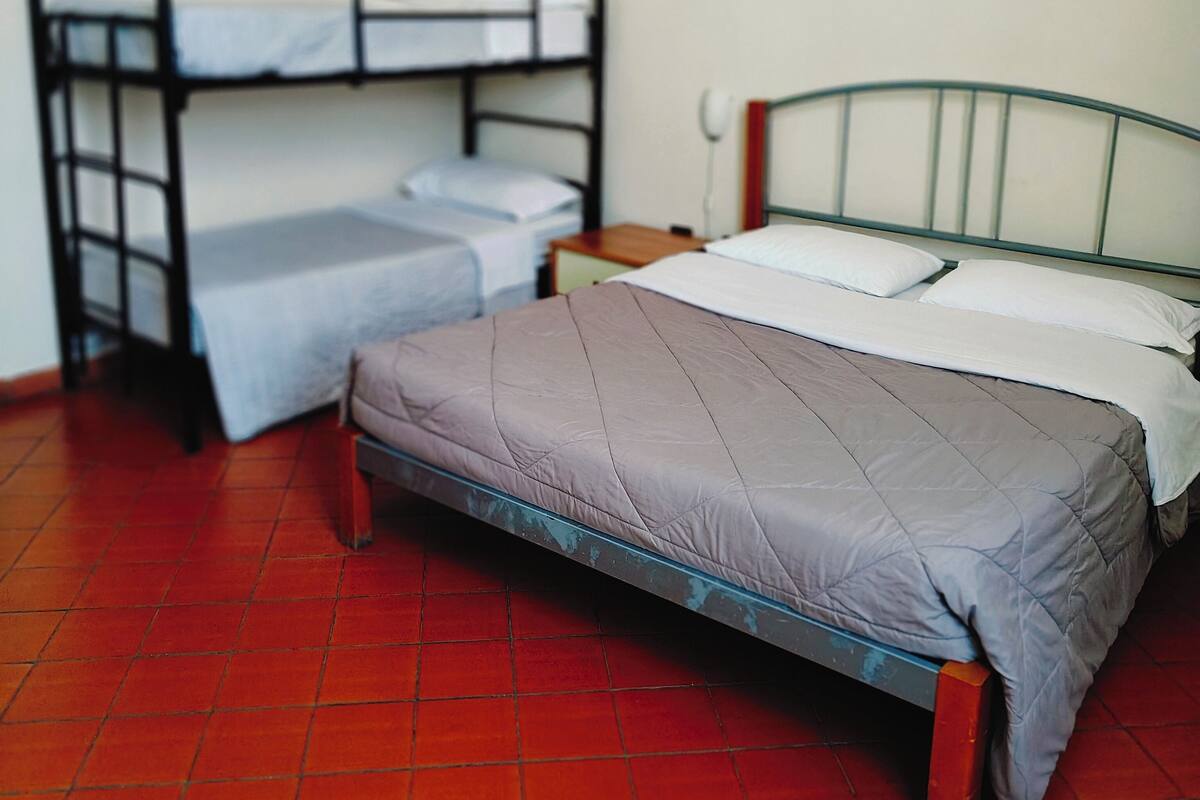 A room with a bunk bed, a single bed, a nightstand, and a red tiled floor.