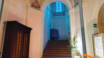 A hallway with a staircase leading to a blue-lit room, a dark wooden cabinet, and a framed certificate on a stand.