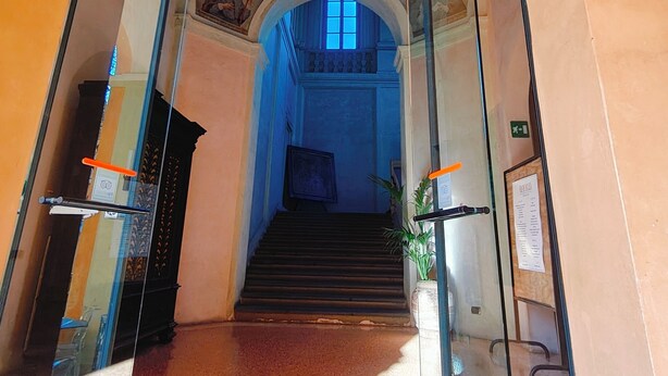 A glass-enclosed entrance with a staircase leading to a higher level. - Student's Hostel della Ghiara (Reggio nell'Emilia)