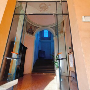 Una entrada con paredes de vidrio y una escalera que sube a un nivel superior.
