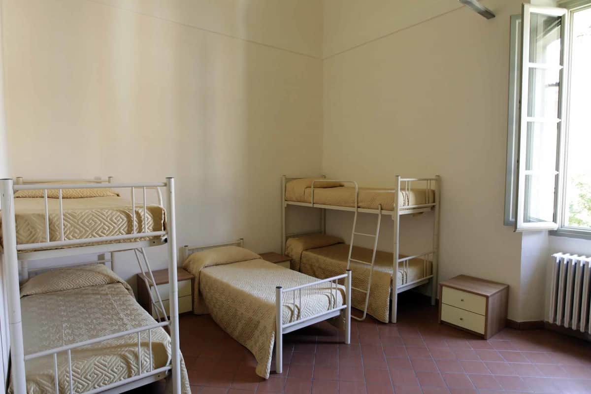 A dormitory room with bunk beds, a small bedside table, and a radiator.