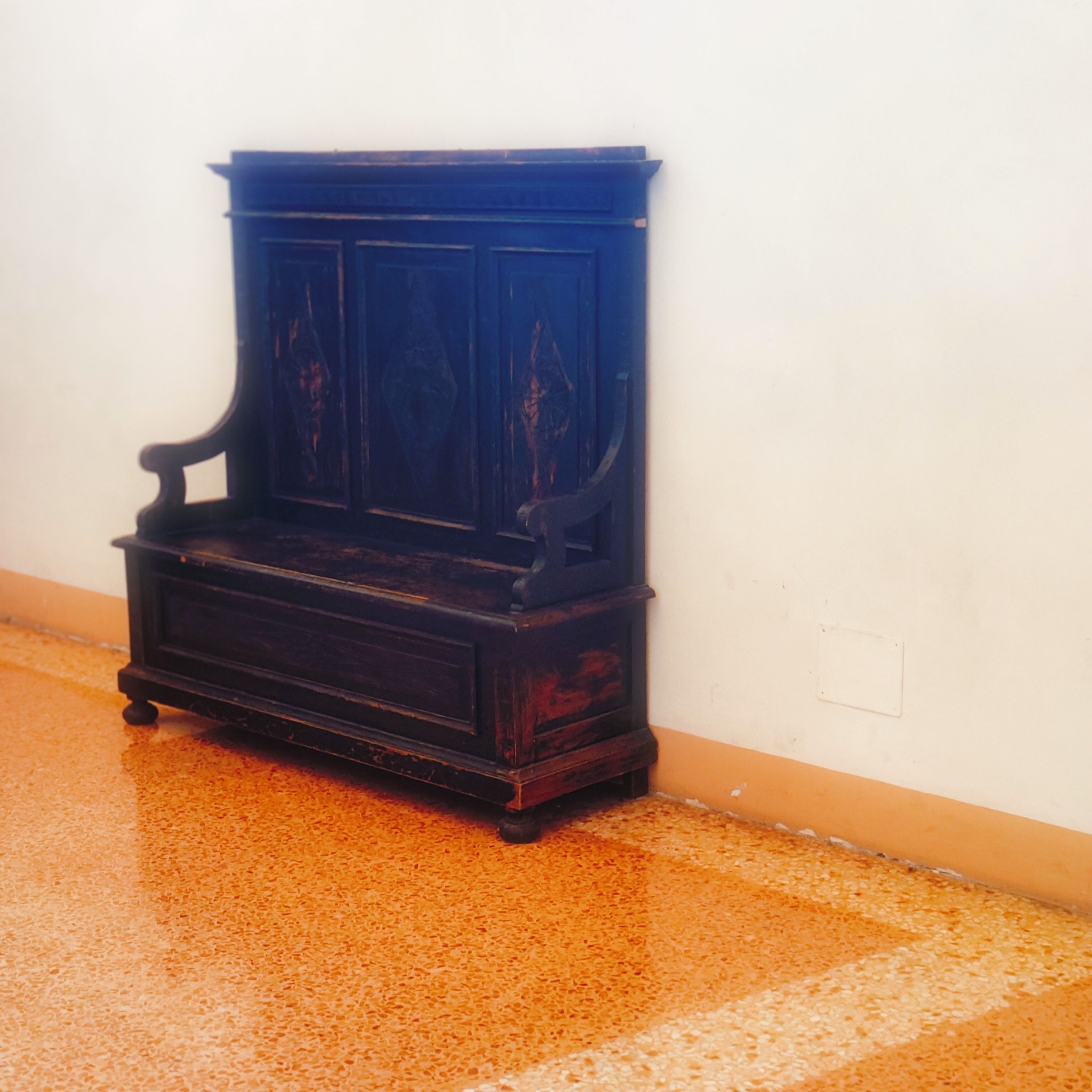 Un banco de madera oscura con detalles tallados sobre un muro liso.